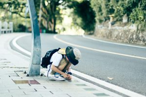 Young boy crouching on a sidewalk, inspecting something. Outdoor city environment.